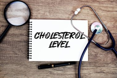 Not defterine steteskop ve ahşap zemin üzerinde büyüteç ile kolesterol düzeyi metni yazıldı