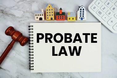 Ev modeli, hesap makinesi ve mermer zemin üzerinde tokmak bulunan not defterine yazılan Vasiyet Kanunu metni