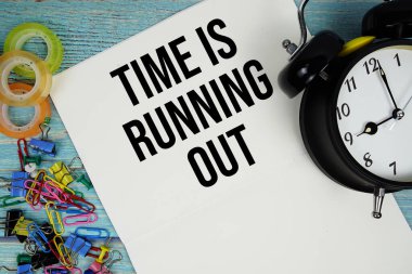 Zaman tükeniyor alarm saati ve mavi ahşap bir yüzey üzerindeki renkli ofis malzemeleriyle.