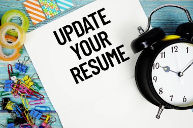 Ofis malzemeleriyle çevrili bir kağıt ve mavi ahşap bir yüzey üzerindeki bir saat üzerindeki özgeçmişinizi güncelleyin