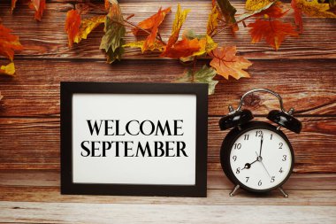Alarm saati ve ahşap arka planda akçaağaç yaprağı süslemesiyle Eylül ayına ait metne hoşgeldiniz