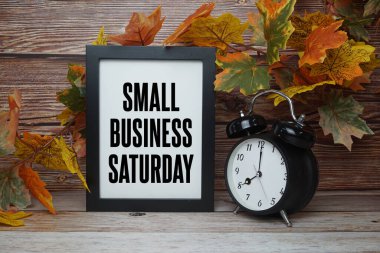 Alarm saati ve ahşap arka planda akçaağaç yaprağı süslemesi olan küçük işletme cumartesi metni