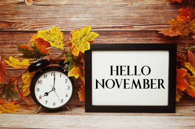 Alarm saati ve ahşap arka planda akçaağaç yaprağı süslemesi olan Kasım metni