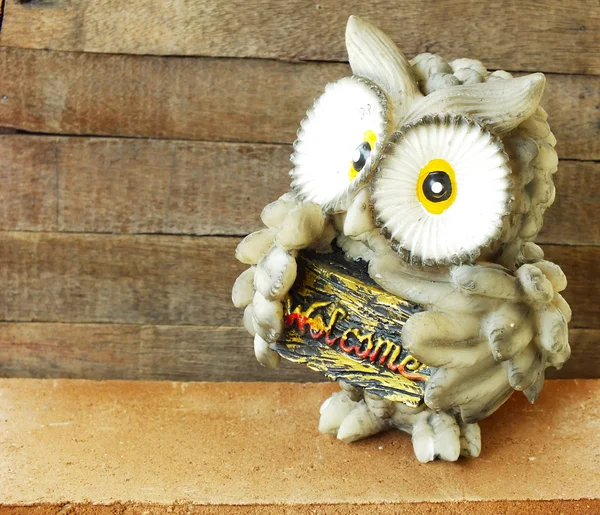 statue of owl bird welcome sign on wooden background still life