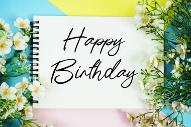 Çiçek süslemeleri ile not defterine yazılan mutlu yıllar metni çok renkli pastel arka planda yatıyordu