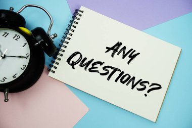 Any Questions text written on notepad with alarm clock flat lay on multicolor pastel background