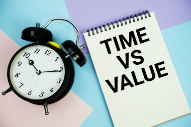 Alarmlı saatin düz olduğu not defterinde yazılan değer metni çok renkli pastel arka planda yatar