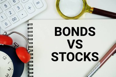 Not defterinde alarm saati ve beyaz arkaplanda hesap makinesi ile yazılmış hisse senetlerine karşı senetler