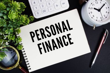 Alarm saati, büyüteç ve siyah zemin üzerine hesap makinesi ile not defterine yazılmış kişisel finans metni