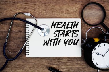 Sağlık seninle başlar not defterine steteskop, büyüteç ve ahşap arka planda çalar saat ile yazılmış metinler