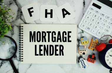Ev modeli, hesap makinesi, mermer zemin üzerindeki büyüteç ve alarm saati ile birlikte not defterine yazılan FHA mortgage Tefecisi metni