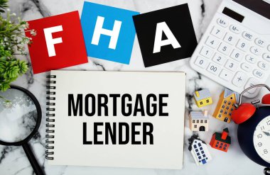 Ev modeli, büyüteç, hesap makinesi ve mermer zemin üzerindeki alarmlı saat ile birlikte not defterine yazılmış FHA mortgage Lender metni