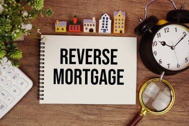 Ev modeli, büyüteç, hesap makinesi ve ahşap zemin üzerindeki alarm saatiyle birlikte not defterine yazılan ipotek metnini tersine çevir