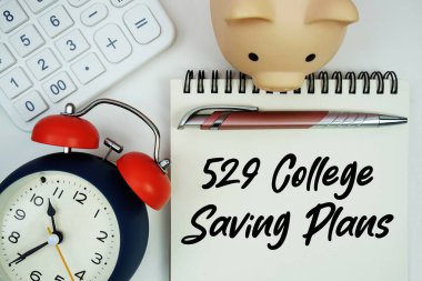 529 Kolej Tasarruf Planı. Hesap makinesi, kumbara ve alarm saatiyle yazılmış not defteri.