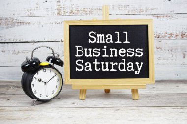 Küçük İşletme Cumartesi metni tahtaya yazıldı ve ahşap zemin üzerinde çalar saat var.