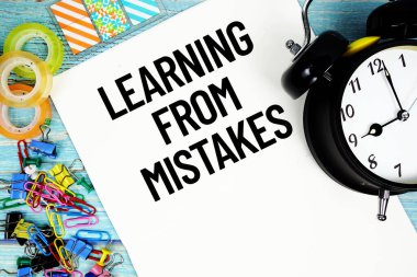 Ofis malzemeleri ve mavi ahşap bir yüzey üzerindeki bir saatle çevrili bir kağıttaki hatalardan ders çıkarmak.