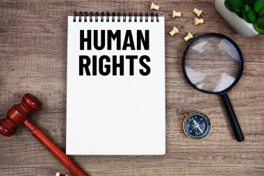 Tahta tokmak ve büyüteçle not defterine yazılan insan hakları mesajı ahşap zemin üzerinde yatıyordu.