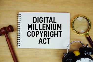 DMCA Dijital Milenyum Telif Hakkı Yasası not defterine kalem, alarm saati ve tahta zemin üzerinde yargıç tokmağı ile yazılmış metin