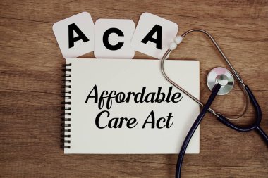 ACA Ekonomik Bakım Yasası metni, not defterine steteskop ile ahşap zemin üzerine yazılmış.