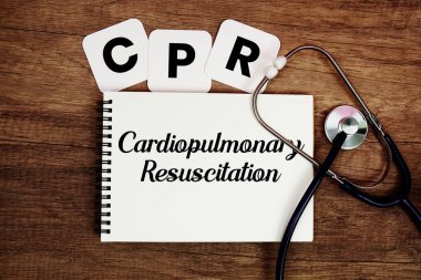 Kalp masajı kardiyopulmoner resüsitasyon metni. Not defterine steteskop ile ahşap arka planda yazılmış.
