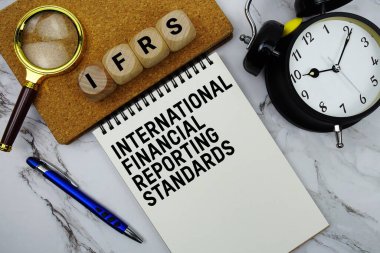 IFRS Uluslararası Mali Raporlama Standartları not defterine mermer zemin üzerinde büyüteç ve alarm saati ile yazılmış metinler