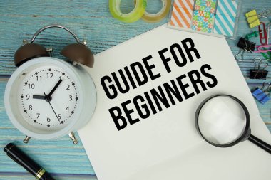 Yeni başlayanlar için kılavuz ofis malzemeleri, bir büyüteç ve mavi ahşap bir yüzey üzerinde bir saat ile çevrili bir kağıt üzerinde metin