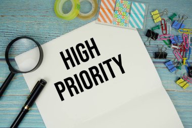 Ofis malzemeleri ve mavi ahşap bir yüzey üzerindeki büyüteçle çevrili bir kağıtta yüksek öncelikli metin.