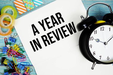 Çalar saat ve mavi ahşap bir yüzey üzerindeki renkli ofis malzemeleriyle gözden geçirilmiş bir yıl.