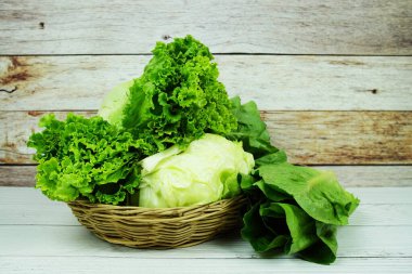 Fresh raw Iceberg, Romaine and Green Cos lettuces in bamboo basket on wooden background