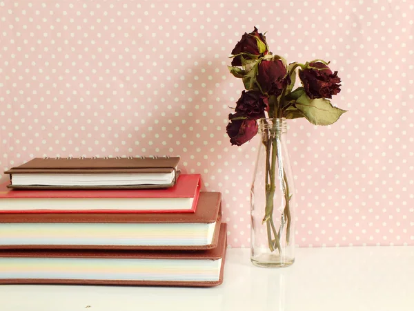 Vida morta de rosas secas e pilha de notebook em fundo de bolinhas rosa — Fotografia de Stock