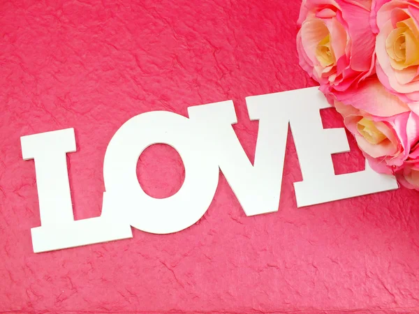 Palavra de amor no fundo rosa com flores de rosas rosa artificiais — Fotografia de Stock