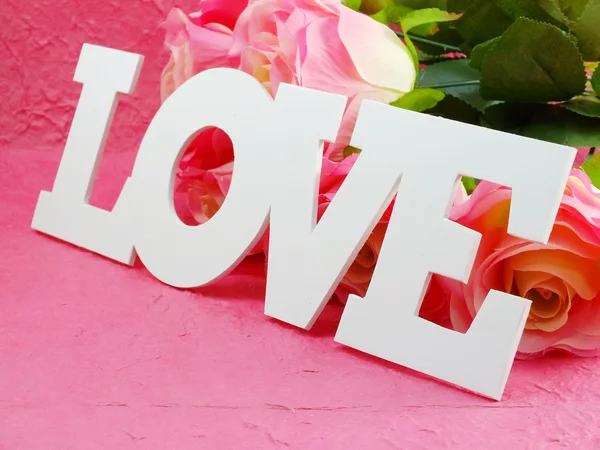 Palavra de amor no fundo rosa com flores de rosas rosa artificiais — Fotografia de Stock