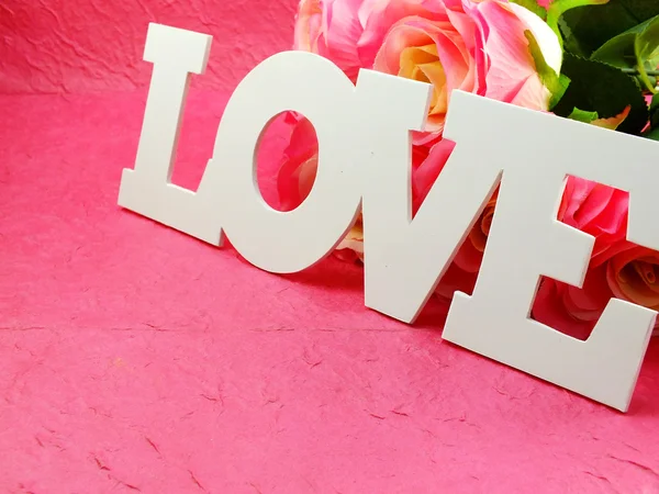 Любовное слово на розовом фоне с искусственными розовыми цветами — стоковое фото