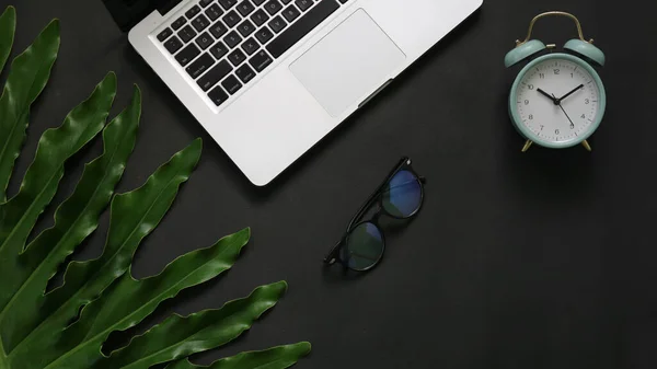 Green leaves laptop alarm clock eyeglass on black background 