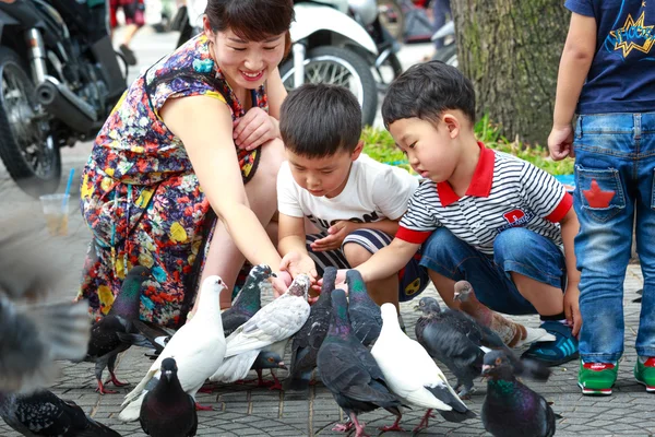 Hochiminh City, Vietnam - 14 Temmuz 2015: iki bebek erkek ve bir kadın Saigon sokaklarında ellerinde güvercin besleme