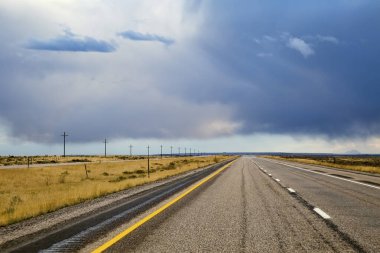 Boş bir çift şeritli Amerikan orta batı otoyolu uzanıyor. Fırtına bulutları tepemizde tehdit oluştururken..