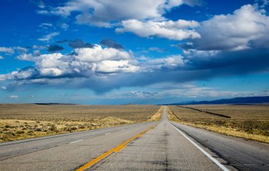 Wyoming 'de boş bir 26. yol mesafeye uzanıyor. Tepemizde dramatik bulutlar.