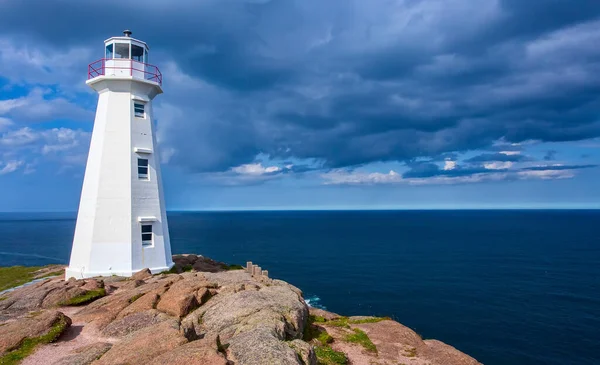 The Cape Spear Lighthouse in Newfoundland, under a dramatic blue cloud sky.