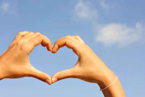 Female hands making the heart on the sky background Stock Image