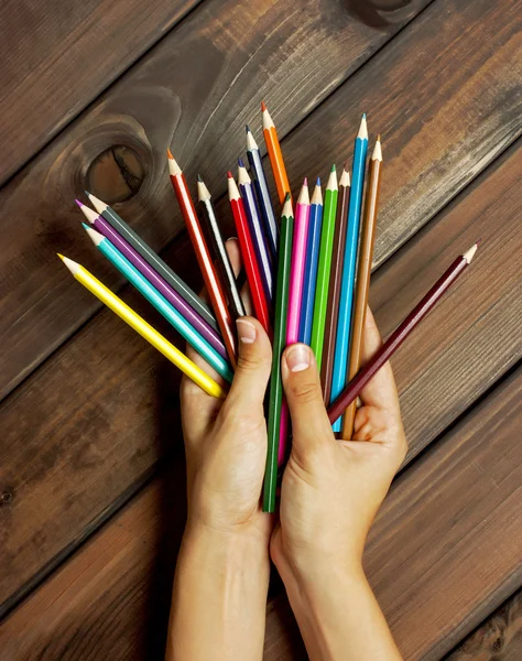 Zestaw kolorowych ołówków w ręce kobiece na tle ciemnego drewna stoły — Zdjęcie stockowe
