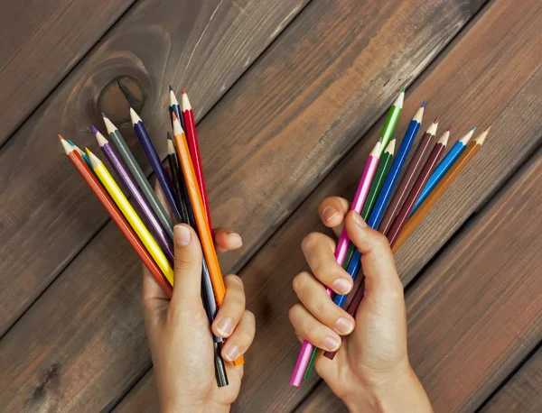 Набір кольорових олівців у жіночих руках на тлі темних дерев'яних столів — стокове фото