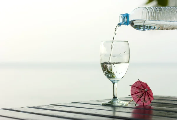 Glas rent vatten på ett mörkt bord på stranden med en Palm — Stockfoto