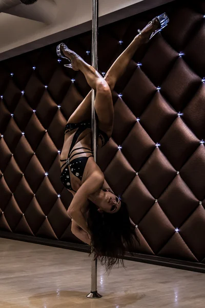 Young beautiful girl in a black suite doing acrobatics on a pole — Stock Photo, Image