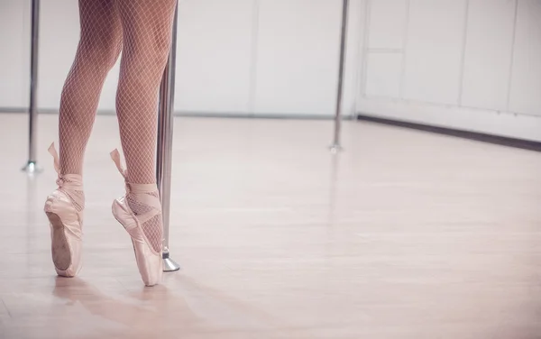 Una ballerina di danza classica in piedi a Pointe vicino al palo nello studio vuoto con pavimento in legno. primo piano . — Foto Stock