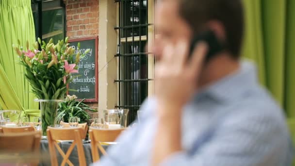 Un uomo che parla al cellulare al ristorante, con una telecamera fissa. — Video Stock