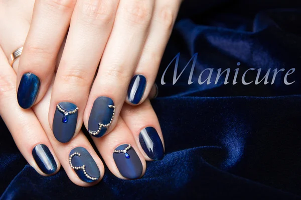 Manicure francês - belas mãos femininas cuidadas com manicura azul com strass em fundo azul escuro — Fotografia de Stock