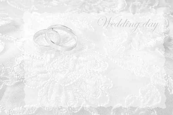 Anéis de casamento no cartão de casamento, em um vestido de casamento branco — Fotografia de Stock