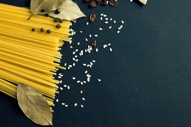Pişmemiş spagetti ve defne yaprağı, kızamık, biber, susam siyah-mavi ahşap arka plan, metin için üstten görünüm yer