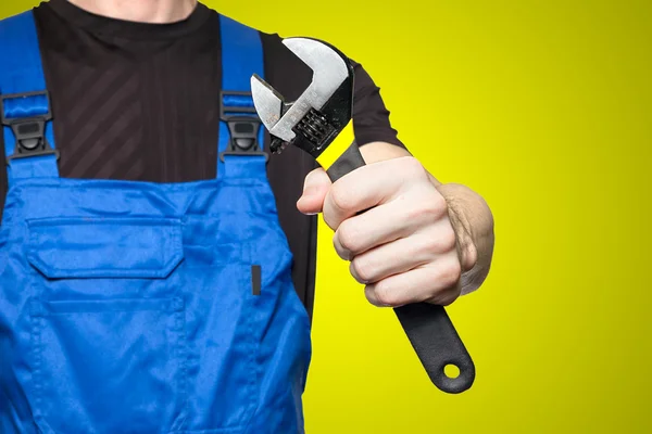 Mechaniker in Arbeitskleidung hält einen Schraubenschlüssel in der Hand, isoliert auf gelbem Hintergrund — Stockfoto