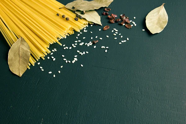 Spaghettis crus et feuille de laurier, épine-vinette, poivre, graines de sésame sur fond bois noir-bleu-vert, vue du dessus place pour le texte — Photo